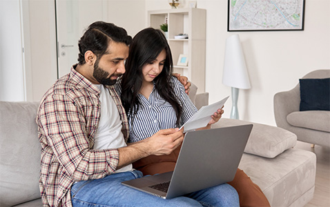 young Indian couple sitting on a couch reading from a paper bill with a laptop